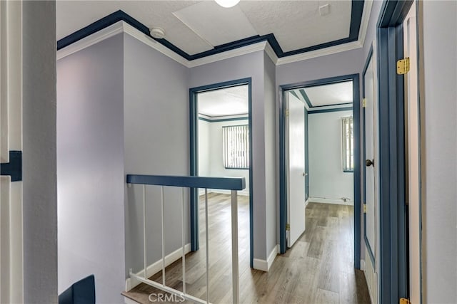 hall with crown molding, a textured ceiling, an upstairs landing, light wood-type flooring, and baseboards