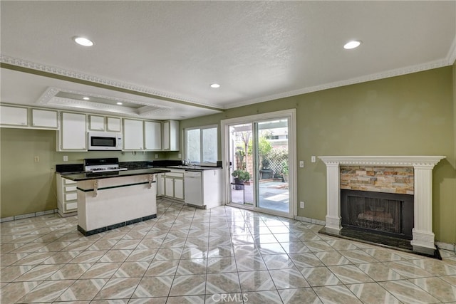 kitchen featuring dark countertops, a raised ceiling, white cabinets, a kitchen island, and white appliances