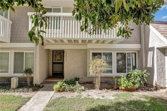 view of exterior entry featuring a balcony and stucco siding