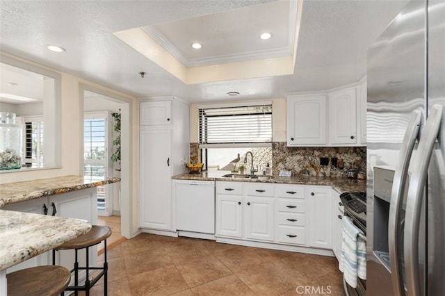 kitchen featuring stainless steel appliances, a sink, light stone countertops, a tray ceiling, and crown molding