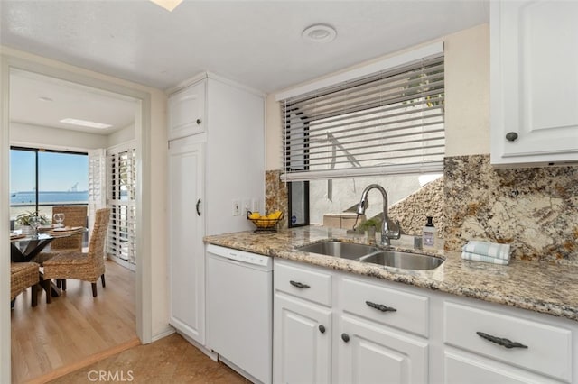 kitchen with white dishwasher, white cabinetry, backsplash, and a sink