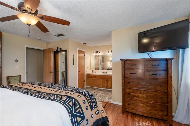 bedroom featuring visible vents, a textured ceiling, ensuite bathroom, and wood finished floors