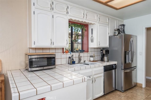 kitchen with tile countertops, a sink, white cabinets, appliances with stainless steel finishes, and decorative backsplash