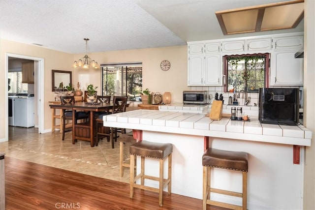 kitchen with a breakfast bar area, white cabinets, hanging light fixtures, tile counters, and stainless steel microwave