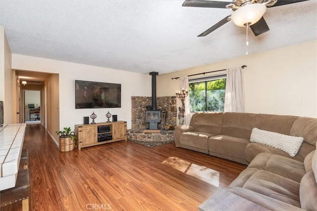 living room with a textured ceiling, wood finished floors, a wood stove, and a ceiling fan