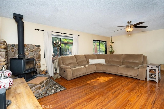 living area featuring a textured ceiling, wood finished floors, a wood stove, and a ceiling fan