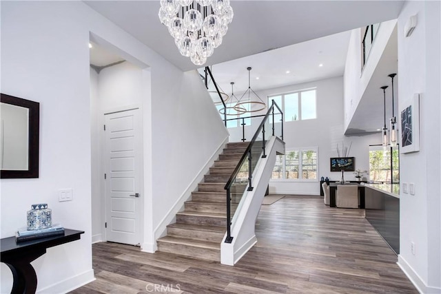 stairs with baseboards, a towering ceiling, wood finished floors, an inviting chandelier, and recessed lighting