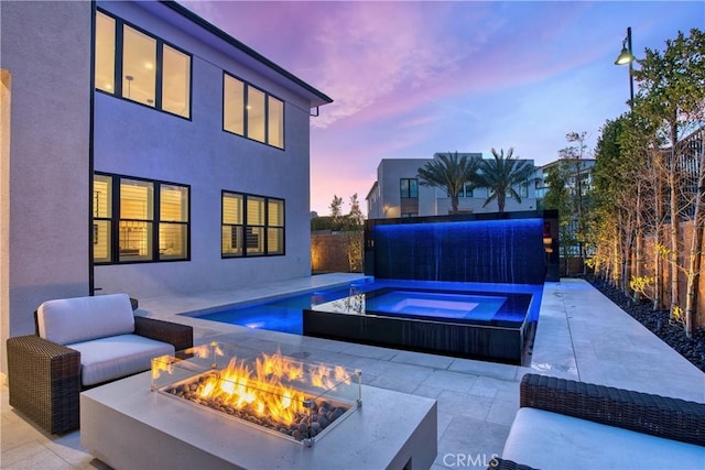 patio terrace at dusk with an in ground hot tub, fence, and an outdoor living space with a fire pit