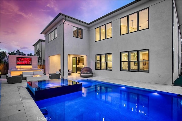 back of house at dusk featuring an outdoor living space with a fire pit, a patio area, an outdoor pool, and stucco siding