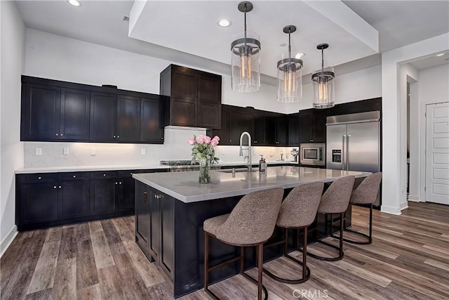 kitchen with built in appliances, a breakfast bar area, a sink, light countertops, and dark wood-style floors