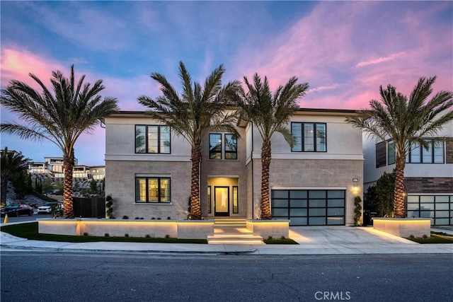 modern home featuring stone siding, driveway, an attached garage, and stucco siding