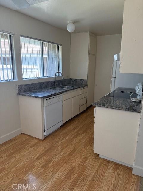 kitchen featuring white appliances, a sink, white cabinetry, baseboards, and light wood-type flooring