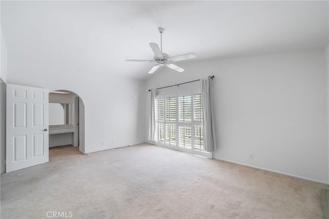 unfurnished bedroom featuring arched walkways, vaulted ceiling, carpet, and a ceiling fan