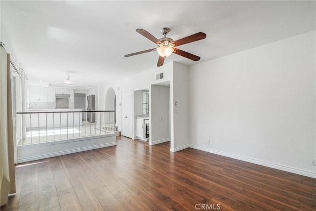 spare room with arched walkways, visible vents, dark wood-type flooring, a ceiling fan, and baseboards