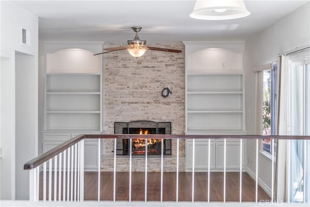 unfurnished living room with built in shelves, a fireplace, wood finished floors, visible vents, and a ceiling fan