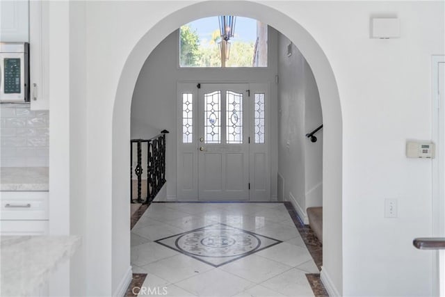 foyer with arched walkways and baseboards