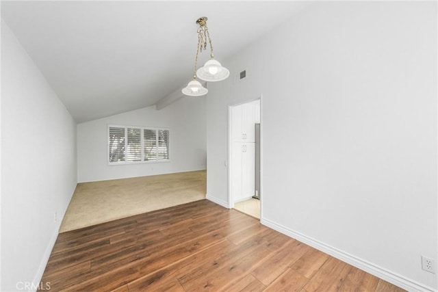 empty room featuring visible vents, baseboards, vaulted ceiling, and wood finished floors