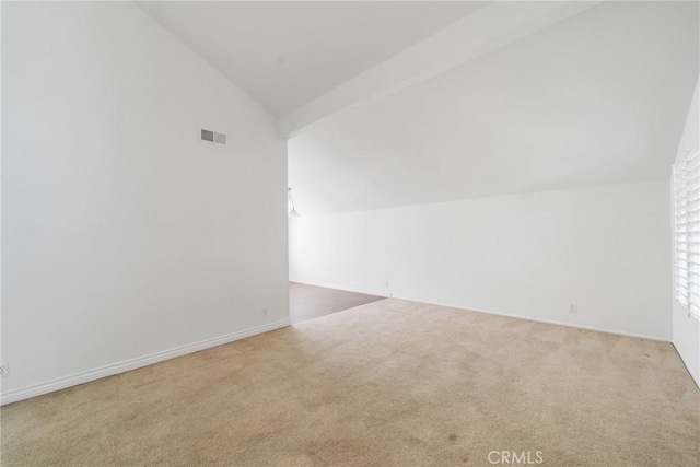 empty room with carpet, visible vents, and vaulted ceiling