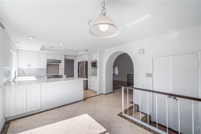 kitchen with arched walkways, stainless steel appliances, decorative backsplash, a sink, and under cabinet range hood