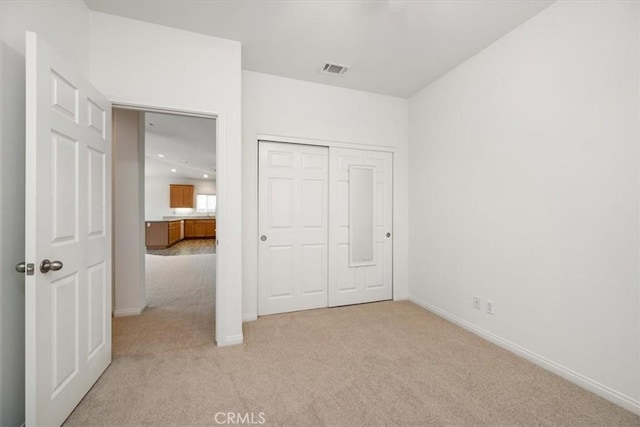 unfurnished bedroom featuring light carpet, a closet, visible vents, and baseboards