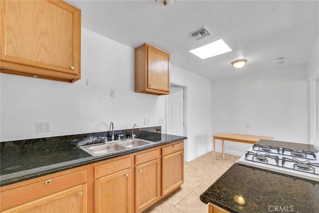 kitchen featuring light tile patterned floors, a sink, visible vents, dark stone counters, and stovetop