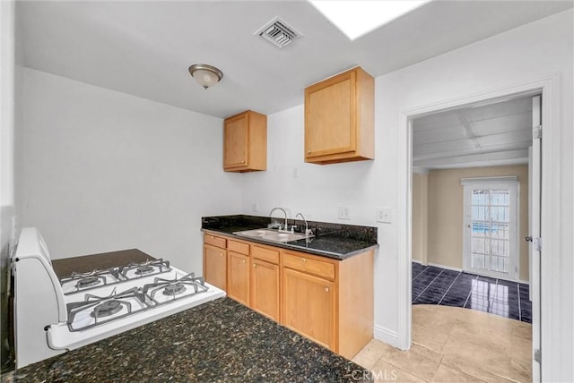 kitchen featuring a sink, visible vents, dark stone counters, light brown cabinetry, and gas range