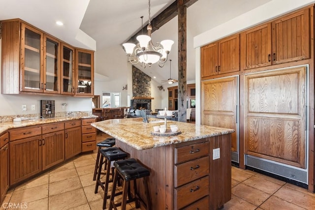 kitchen with a breakfast bar, brown cabinets, lofted ceiling with beams, glass insert cabinets, and a kitchen island with sink