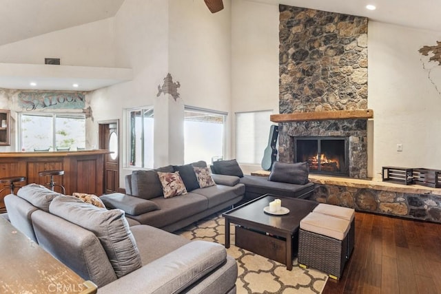 living room with visible vents, wood-type flooring, a stone fireplace, high vaulted ceiling, and recessed lighting