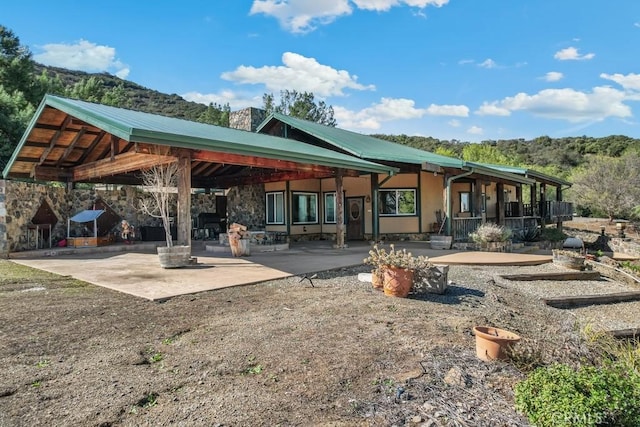 rear view of house with stone siding, a patio area, metal roof, and a chimney