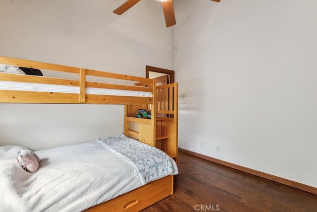 bedroom with a towering ceiling, ceiling fan, baseboards, and wood finished floors