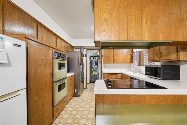 kitchen featuring tile countertops, a peninsula, appliances with stainless steel finishes, brown cabinets, and light floors