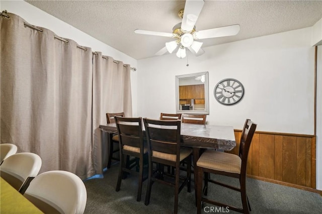 dining area with wooden walls, wainscoting, ceiling fan, carpet, and a textured ceiling