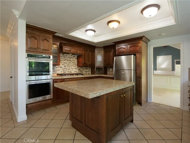 kitchen featuring ornamental molding, a tray ceiling, stainless steel appliances, backsplash, and light tile patterned flooring