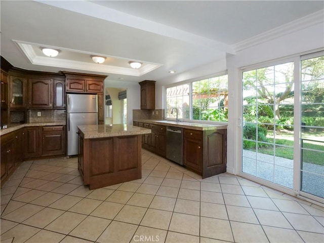 kitchen featuring light tile patterned floors, appliances with stainless steel finishes, a tray ceiling, crown molding, and backsplash