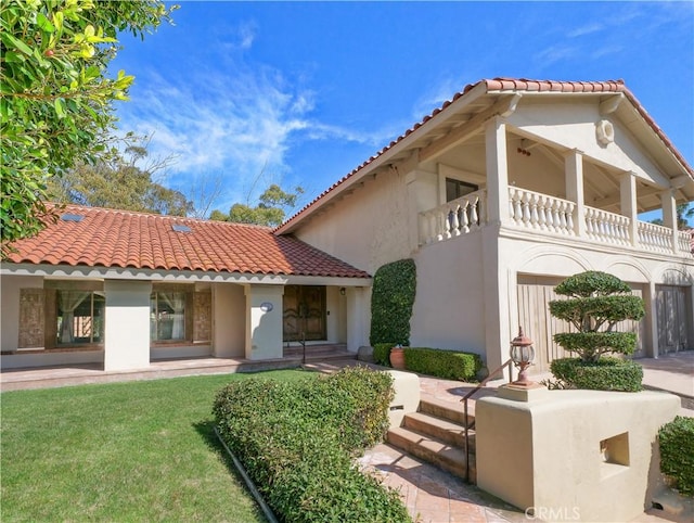 rear view of house with a yard, a tiled roof, a balcony, and stucco siding