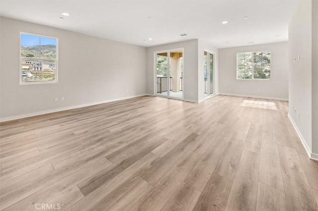 empty room with light wood-style floors, recessed lighting, plenty of natural light, and baseboards