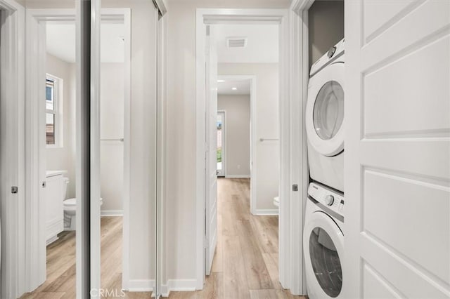 clothes washing area featuring stacked washer / dryer, baseboards, visible vents, and light wood finished floors