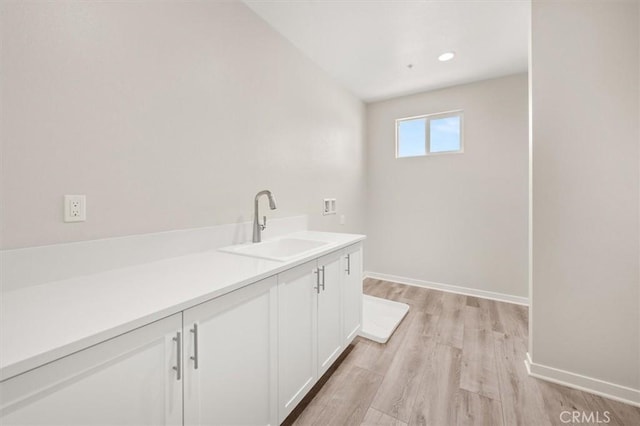 laundry room featuring hookup for a washing machine, cabinet space, a sink, light wood-type flooring, and baseboards