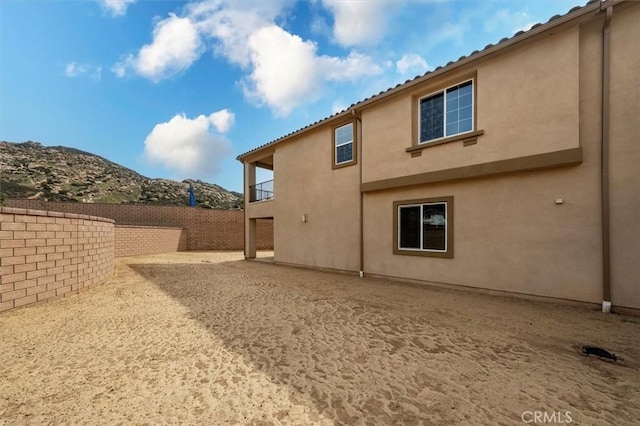 rear view of house with fence private yard, a balcony, a mountain view, stucco siding, and a patio area