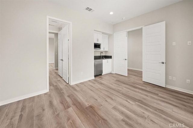 unfurnished room with a sink, light wood-style flooring, visible vents, and baseboards