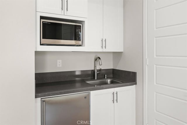 kitchen with dark countertops, white cabinetry, stainless steel appliances, and a sink