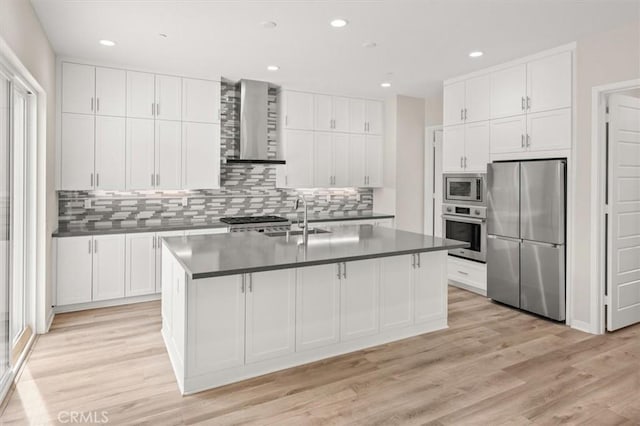 kitchen featuring a sink, appliances with stainless steel finishes, wall chimney range hood, and white cabinets