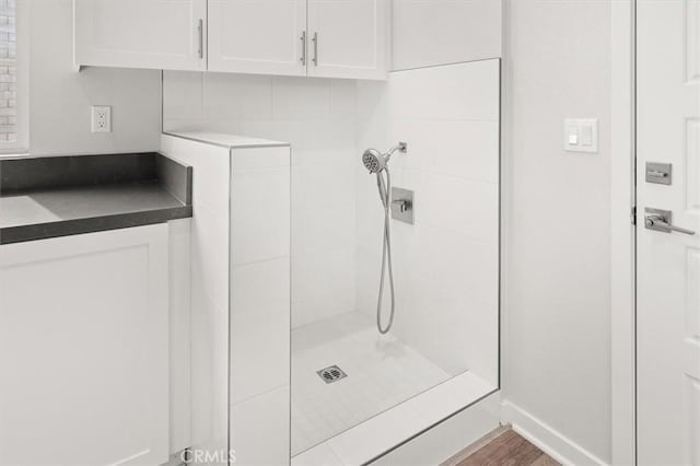 full bathroom with tiled shower, baseboards, and wood finished floors