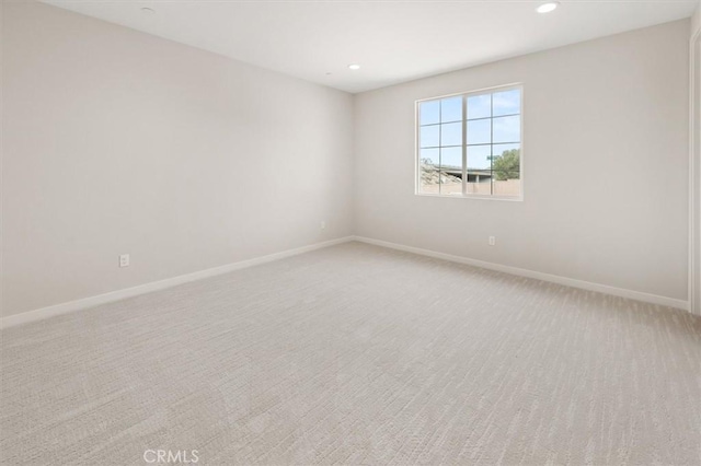 spare room featuring recessed lighting, light colored carpet, and baseboards