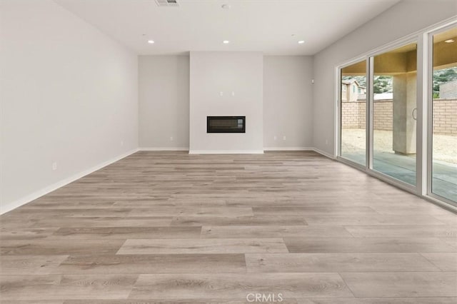 unfurnished living room featuring light wood finished floors, baseboards, and a glass covered fireplace