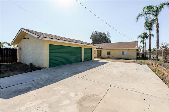 view of front of property featuring stucco siding, a detached garage, an outdoor structure, and fence