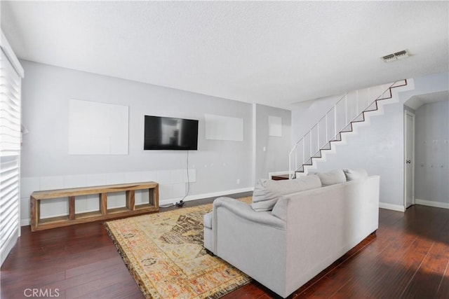 living room featuring dark wood-style flooring, visible vents, stairway, and baseboards