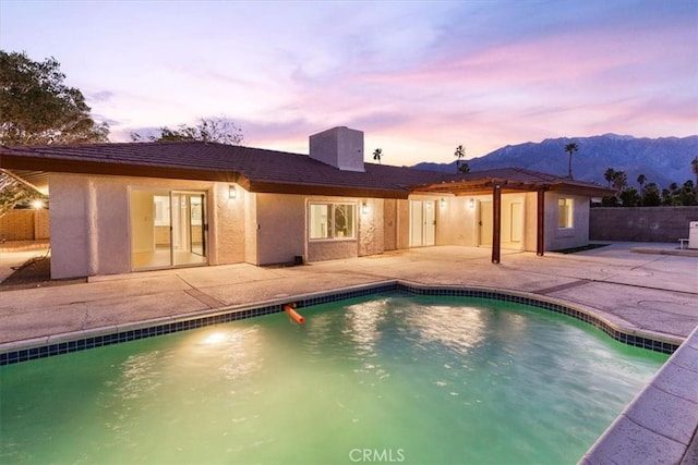 pool at dusk with fence, a mountain view, a fenced in pool, and a patio