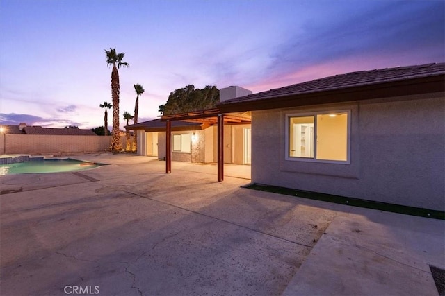 back of house at dusk featuring a patio, fence, a fenced in pool, and stucco siding