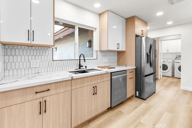 kitchen featuring light wood-style flooring, appliances with stainless steel finishes, light brown cabinetry, washing machine and dryer, and a sink